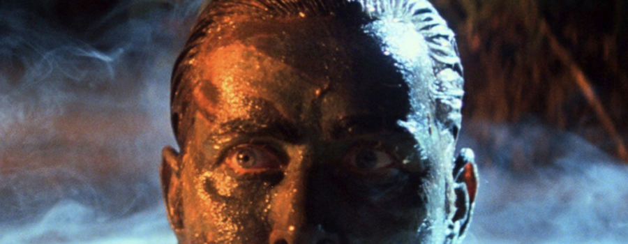 A man rises from a bog, his face covered in mud and substances this editor cannot determine.